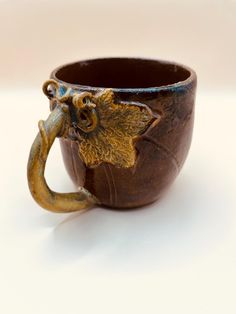 a ceramic cup with an elephant handle on it's side, sitting on a white surface