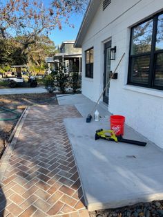 a red bucket sitting on top of a cement slab next to a brick walkway near a house