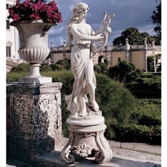 a white statue holding a flute next to a planter with pink flowers in it