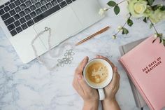 a person holding a cup of coffee in front of a laptop on a marble table