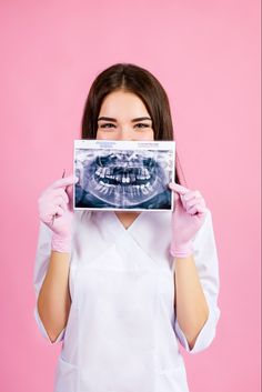 a woman in white shirt and pink gloves holding up an x - ray to her face