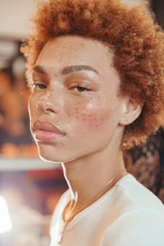 a woman with freckles on her face looking off to the side while wearing a white shirt