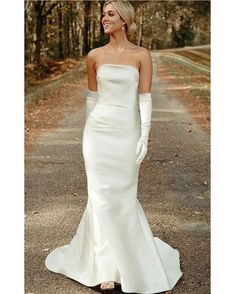 a woman in a white dress is standing on the road with her hands behind her back