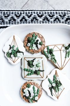 some cookies decorated with flowers and greenery are on a white plate next to a black and white table cloth