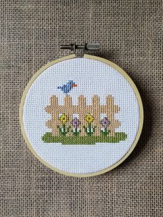 a cross stitch pattern with birds and flowers on the grass in front of a fence