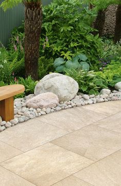 a wooden bench sitting in the middle of a garden next to rocks and plants on either side of it