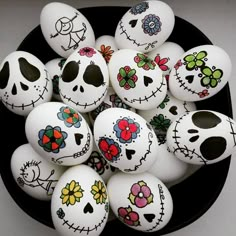 a bowl filled with lots of white eggs covered in painted skulls and flowers on top of a table