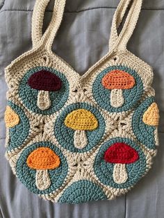 a crocheted bag with mushrooms on it sitting on top of a bed next to a pillow