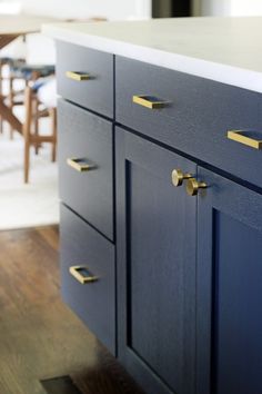 a kitchen with blue cabinets and brass pulls on the handles, along with a dining room table in the background