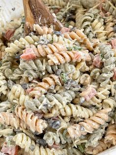 a pasta salad in a white bowl with a wooden spoon