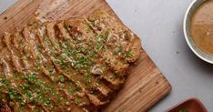 a steak covered in gravy sitting on top of a wooden cutting board