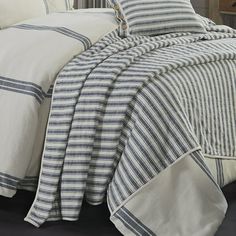 a bed with white and blue striped comforter set on top of it's headboard