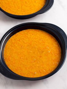 two black bowls filled with soup sitting on top of a white counter next to each other