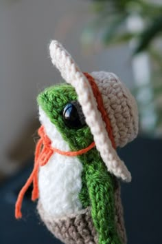 a crocheted green and white stuffed animal wearing a hat with an orange ribbon