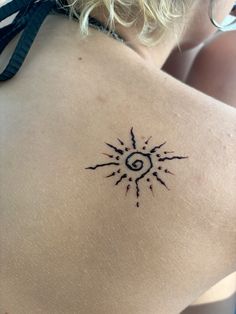 the back of a woman's shoulder with a sun tattoo on her left side