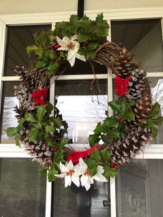 a christmas wreath hanging on the side of a window with pine cones, holly and poinsettis