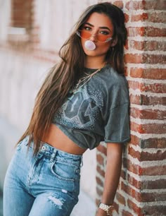 a woman leaning against a brick wall with her tongue out and bubble gum in her mouth