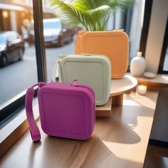 three different colored bags sitting on top of a wooden table next to a large window