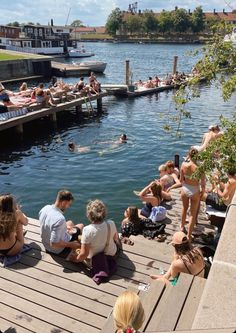 many people are sitting on the dock by the water while others swim in the water