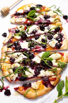 three flatbread pizzas topped with blueberries, cheese and herbs on a white surface