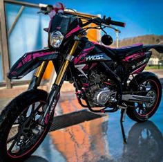 a pink and black motorcycle parked on top of a wet ground next to a building