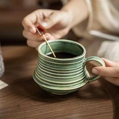 a person is holding a stick in a coffee cup with saucer on the table