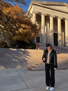 a woman standing in front of a building with columns on the side and steps leading up to it