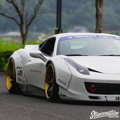 a white sports car with yellow rims driving down the road in front of some trees