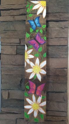 a wooden wall hanging with flowers and butterflies painted on the wood planks in front of it