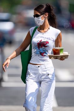 a woman walking down the street wearing a face mask and carrying a tray of food