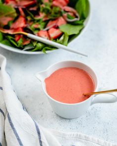 a salad with strawberries and dressing in a white bowl next to a plate of salad