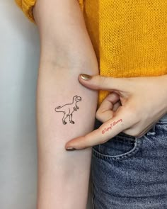 a woman's arm with a small tattoo of a t - rex on it