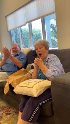 an older couple sitting on a couch with bags in front of them and the woman is screaming