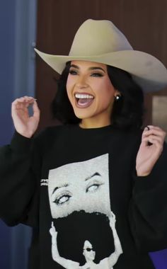 a woman wearing a cowboy hat and black shirt with an image of a woman's face on it