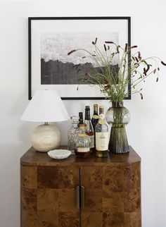 a wooden cabinet with bottles and vases on it next to a framed photograph above