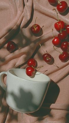 cherries are placed in a white bowl on a pink cloth with the sun shining through