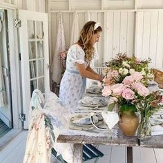 a woman arranging flowers on a table in a room with white walls and wooden floors