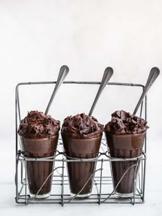 three ice cream cups with chocolate frosting and spoons in them on a wire rack