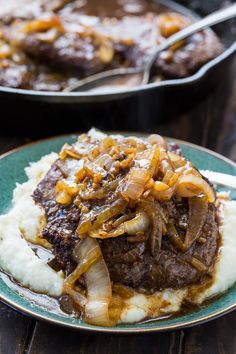 a plate with mashed potatoes, beef and onions on it next to a skillet