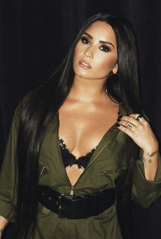 a woman with long dark hair wearing a green shirt and black belted dress, posing for the camera