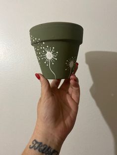 a woman's hand holding up a green cup with white dandelions on it