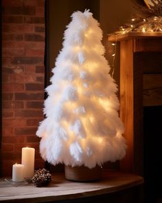 a white christmas tree sitting on top of a wooden table next to a lit candle