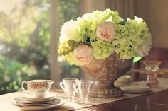 a vase filled with flowers sitting on top of a table next to cups and saucers