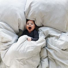 a baby is peeking out from under the covers on a bed that has striped sheets