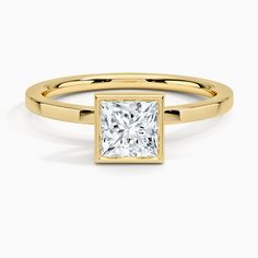 a yellow gold ring with a princess cut diamond in the center, on a white background