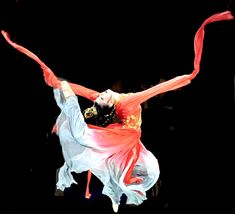 a woman is performing on stage with an orange scarf around her neck and hands in the air