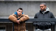 two people standing next to each other behind a fence with their hands on the railing