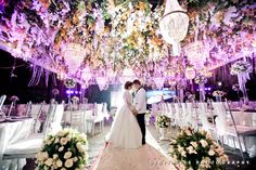 a bride and groom standing under a chandelier with flowers on it at their wedding