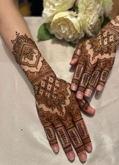 two hands with henna designs on them, one is holding a white flower bouquet