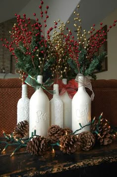 three white bottles with pine cones and red berries in them are sitting on a mantel